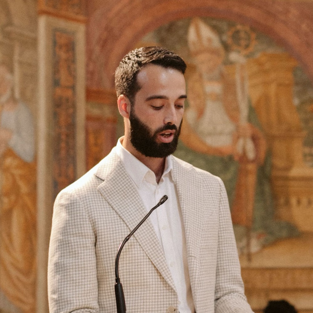 Aluna Rizzoli speaking at a lectern in front of a Renaissance fresco.